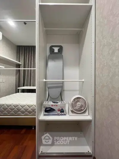 Compact bedroom storage with ironing board and fan, ideal for organized living.