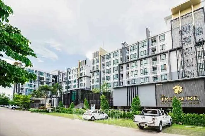 Modern condominium building with lush landscaping and parked cars in front, showcasing urban living.