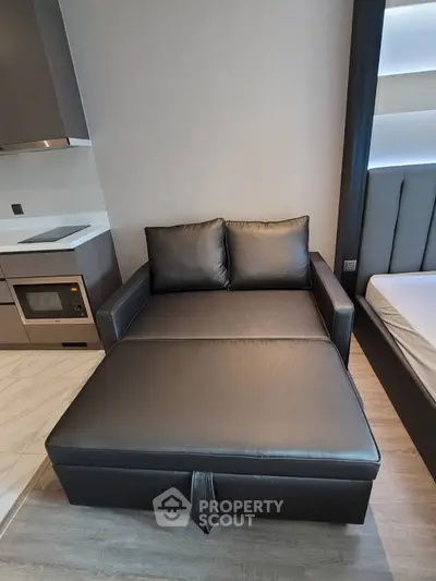 Modern studio apartment with sleek black leather sofa and compact kitchen area.