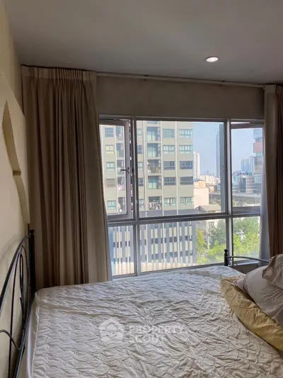 Spacious bedroom with large window offering stunning city view in modern apartment.