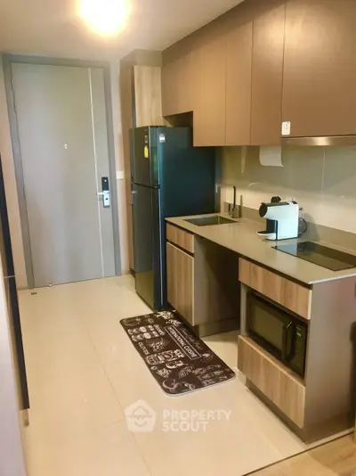 Modern kitchen with sleek cabinetry, fridge, and microwave in compact apartment setting.