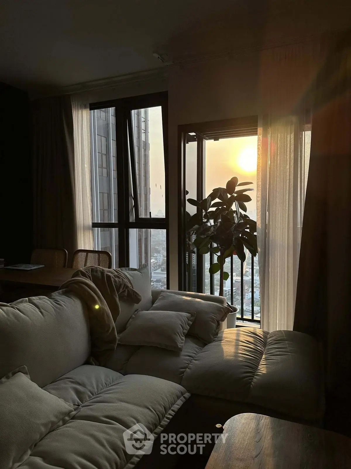 Cozy living room with sunset view, plush sofa, and floor-to-ceiling windows in a modern apartment.