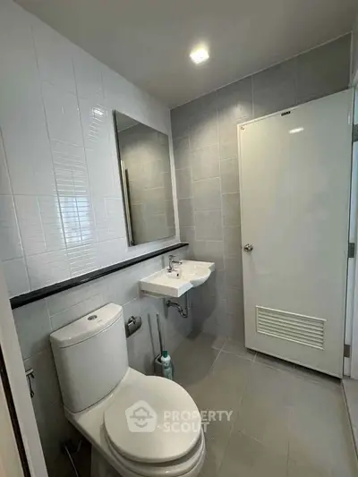 Modern bathroom with sleek fixtures and neutral tiles, featuring a wall-mounted sink and toilet.