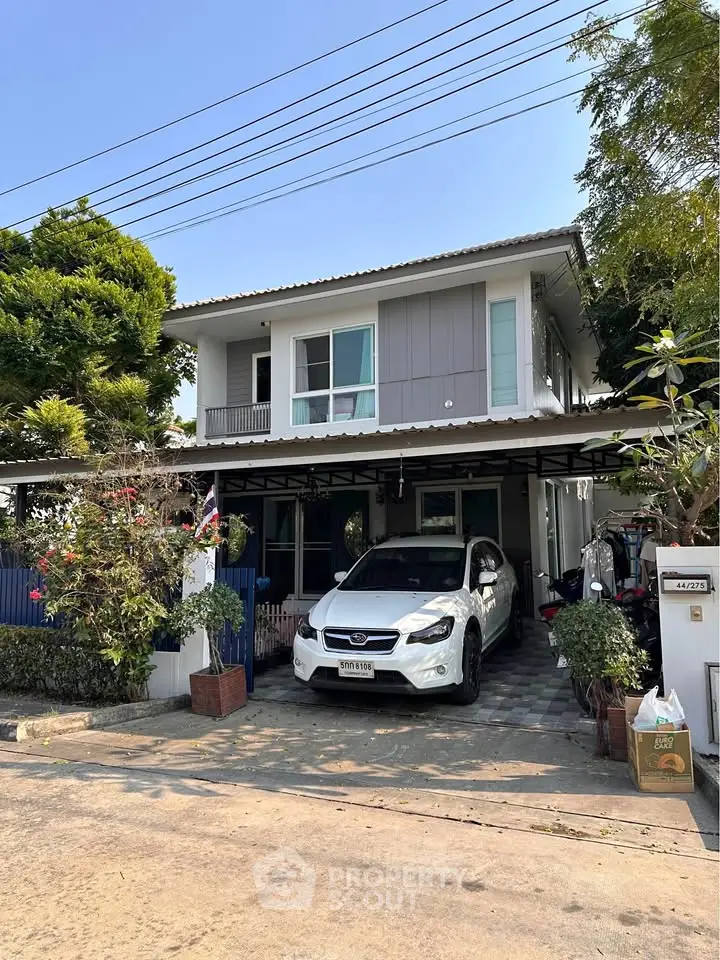 Charming two-story house with carport and lush greenery in suburban setting.