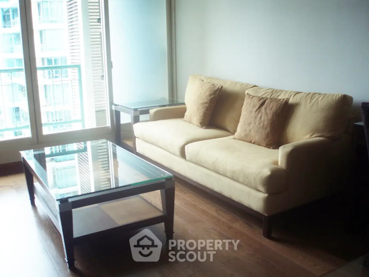 Modern living room with beige sofa and glass coffee table, featuring floor-to-ceiling windows.