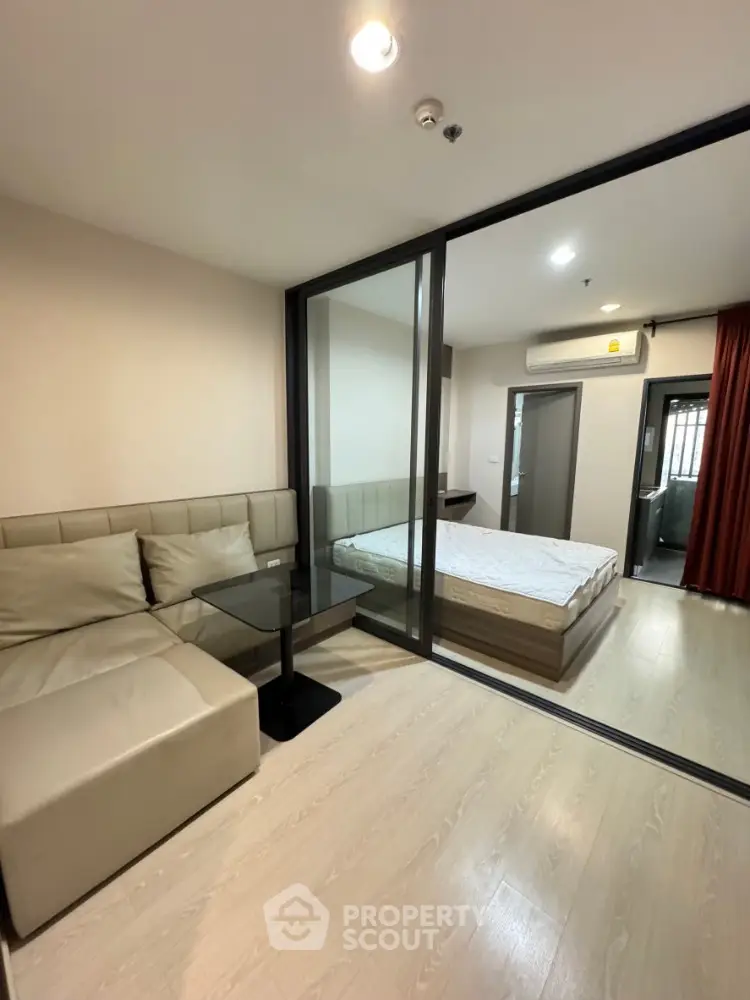 Modern apartment with glass partition separating living room and bedroom, featuring sleek furniture.