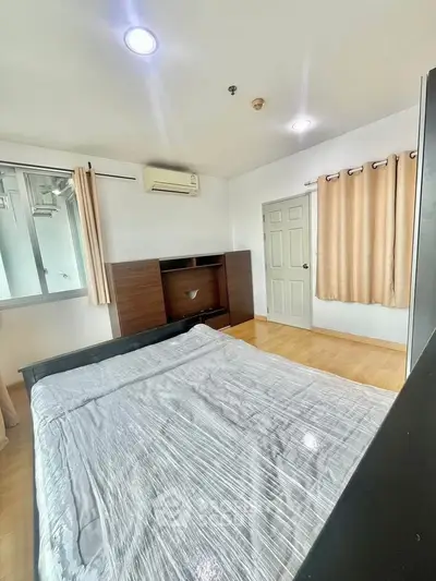 Spacious bedroom with modern furnishings and natural light, featuring air conditioning and wooden flooring.