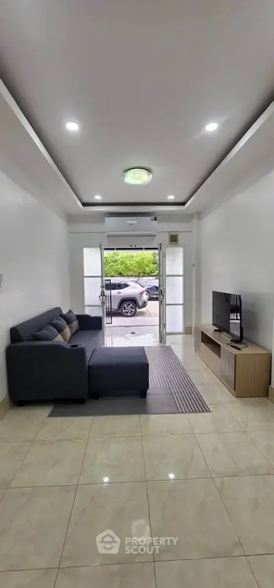 Spacious living room with modern sofa and TV unit, featuring sleek tile flooring and ample natural light.