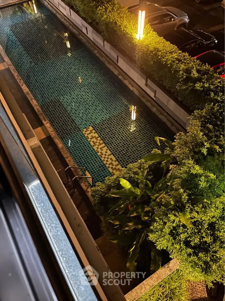 Stunning night view of a modern swimming pool surrounded by lush greenery and ambient lighting.