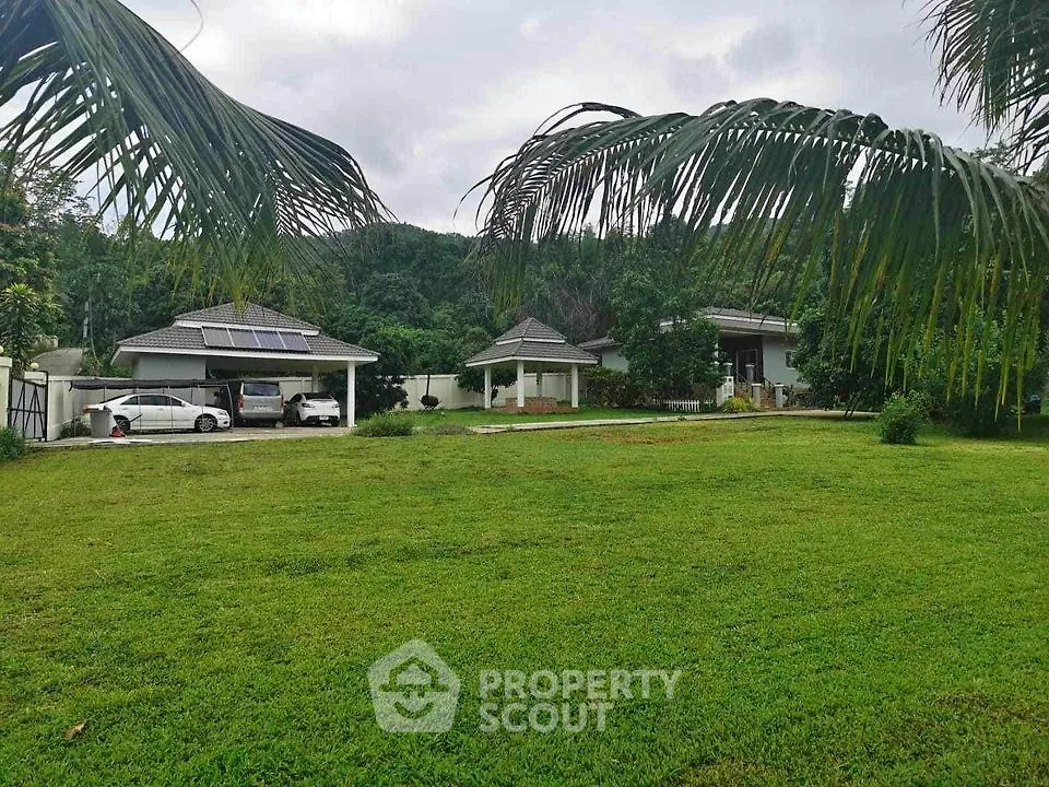 Lush tropical oasis with spacious lawn and twin single-story homes featuring covered parking and serene mountain backdrop.