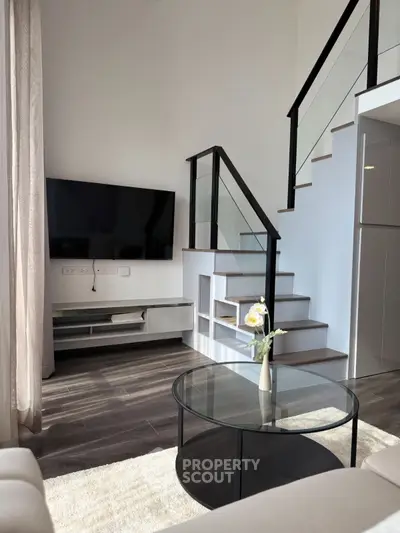 Modern living room with sleek staircase and mounted TV, featuring contemporary design and natural light.