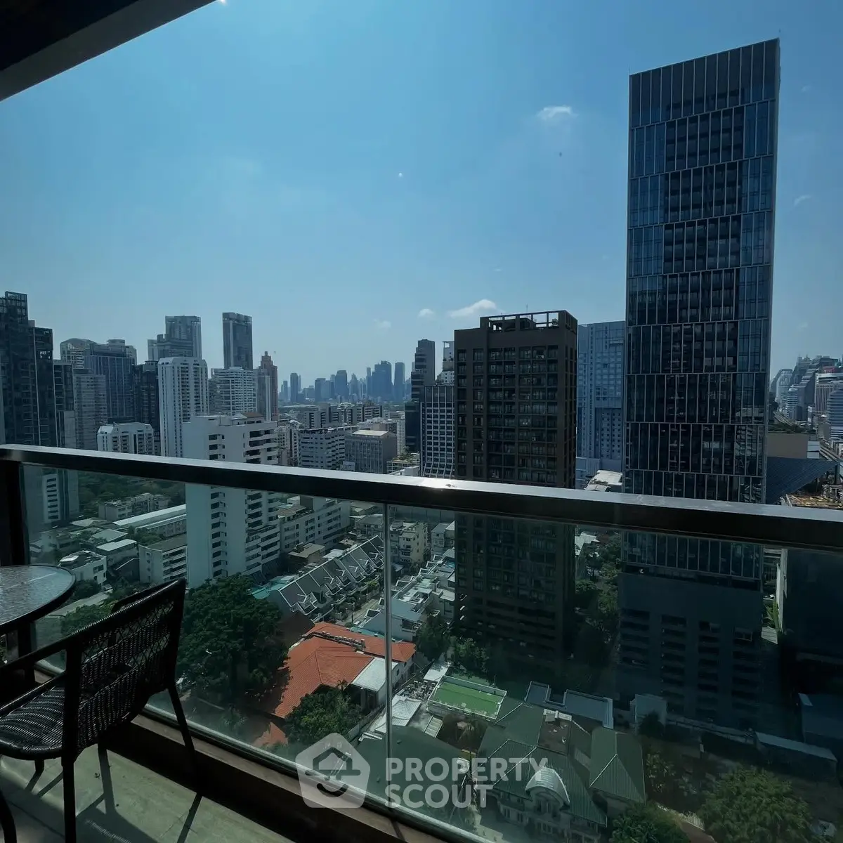Stunning cityscape view from a high-rise balcony with modern skyscrapers and clear blue sky.