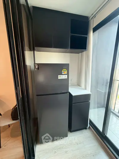 Modern kitchen with sleek black cabinets and a large fridge, featuring a bright window view.