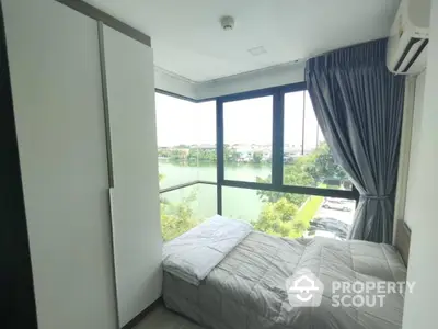 Cozy bedroom with large windows offering stunning river view and modern furnishings.