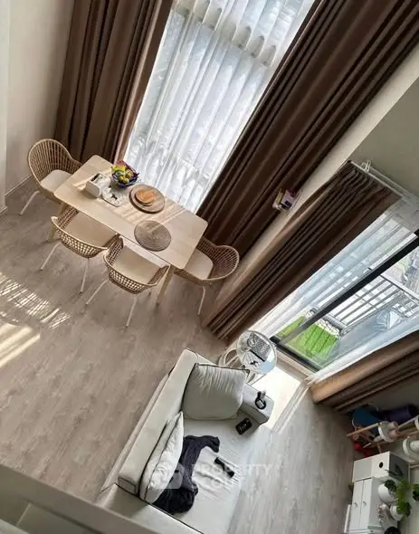 Modern living room with high ceiling and large windows, featuring cozy seating and dining area.