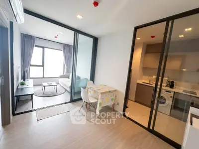 Modern open-plan living room and kitchen with glass partition and natural light.