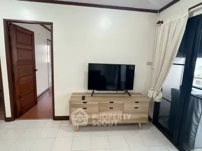 Cozy living room with modern TV stand and flat-screen TV, adjacent to a wooden door and large window.