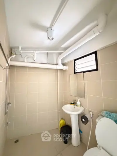 Compact bathroom with modern fixtures and exposed piping, featuring a pedestal sink and toilet.