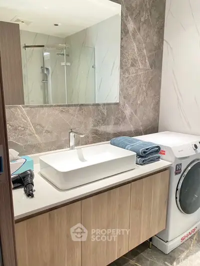 Modern bathroom with sleek vanity and washing machine, featuring elegant marble walls and large mirror.