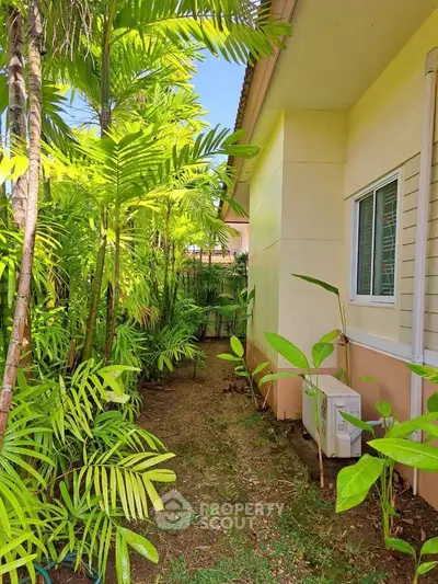 Charming garden view beside a modern house with lush greenery and air conditioning unit.