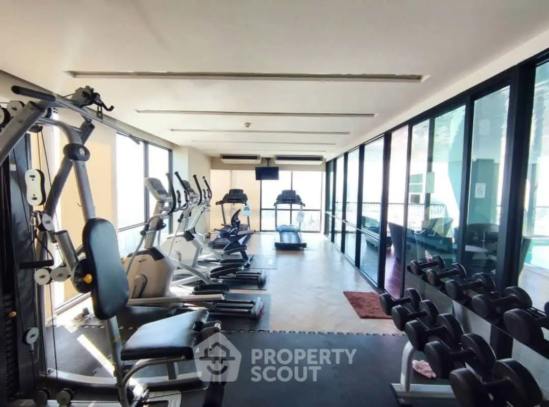 Spacious gym with modern equipment and large windows offering a bright, inviting workout space.