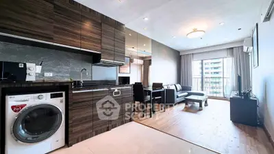 Modern open-plan living room with kitchen featuring sleek cabinetry and washing machine, leading to a balcony with city view.