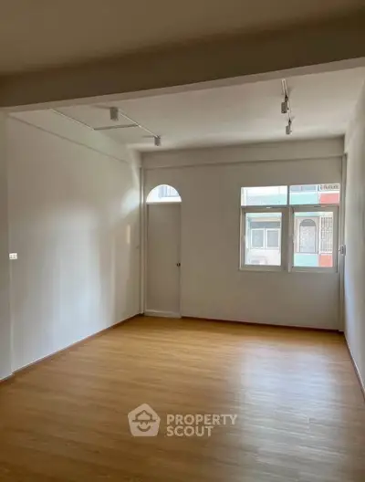 Spacious empty room with wooden flooring and large window, perfect for customization.