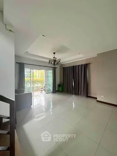 Spacious living room with modern chandelier and large windows leading to balcony.