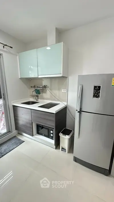 Modern kitchen with sleek cabinetry, double sink, and stainless steel fridge in a bright apartment.