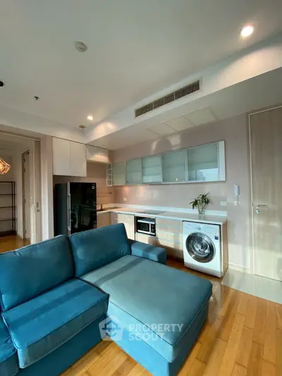 Modern living room with open kitchen, featuring blue sofa and built-in appliances.