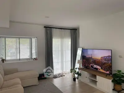 Modern living room with large TV, cozy sofa, and natural light from window and glass door.