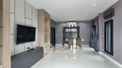 Modern living room with sleek TV setup and dining area, featuring large windows and stylish decor.