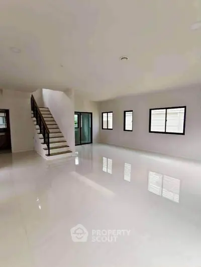 Spacious modern living room with glossy white floors and staircase, ideal for contemporary living.