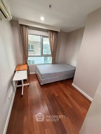 Cozy bedroom with wooden flooring and large window in modern apartment.