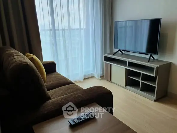 Modern living room with cozy sofa and flat-screen TV, featuring natural light from large windows.