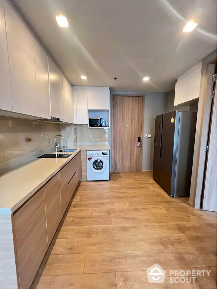 Modern kitchen with sleek cabinetry, washing machine, and spacious fridge in stylish apartment