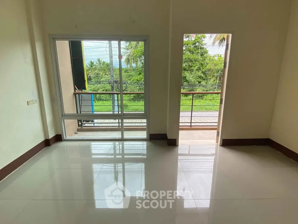 Spacious room with large windows and balcony overlooking lush greenery, perfect for serene living.