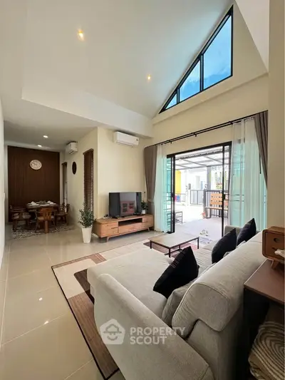Spacious modern living room with high ceiling and large windows, open layout to dining area, stylish decor.