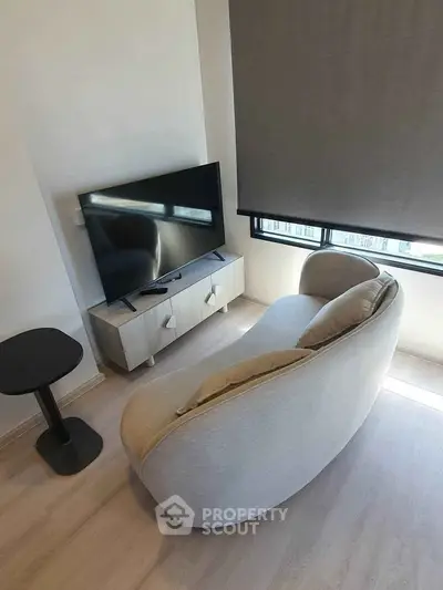 Modern living room with stylish sofa and flat-screen TV, featuring natural light and minimalist decor.