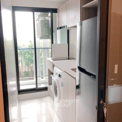 Modern kitchen with washing machine and fridge, featuring sleek cabinetry and large window for natural light.