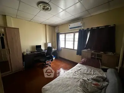 Cozy bedroom with wooden flooring, desk setup, and air conditioning.