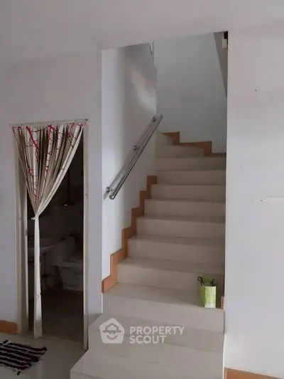 Modern staircase with sleek handrail leading to upper floor, adjacent to a small bathroom with curtain door.