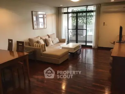 Spacious living room with elegant wooden flooring and modern furniture, featuring a cozy sofa and large windows.