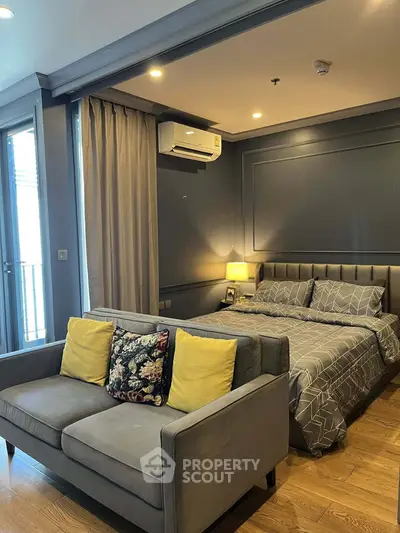 Modern bedroom with stylish decor and cozy seating area, featuring elegant lighting and wooden flooring.