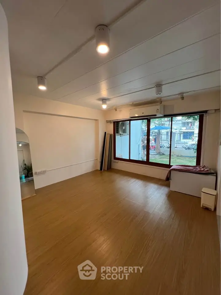Spacious living room with large windows and wooden flooring, offering a serene garden view.