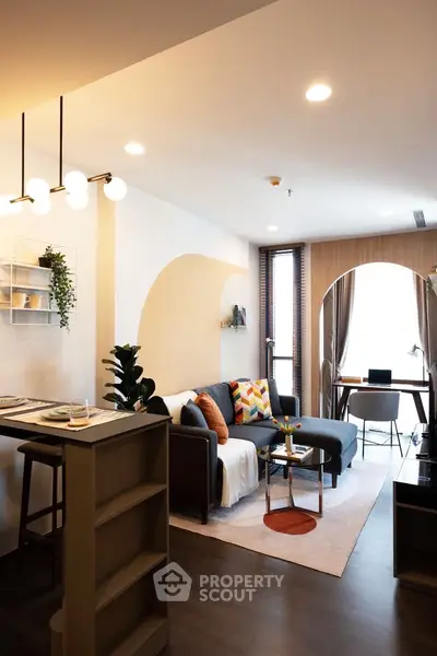 Modern living room with stylish decor and natural light, featuring a cozy sofa and a small dining area.