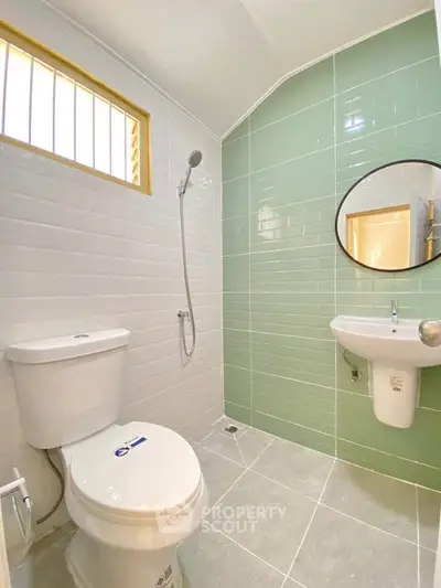 Modern bathroom with green and white tiles, round mirror, and sleek fixtures.