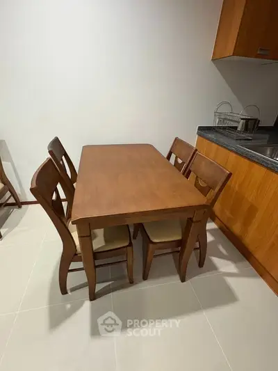 Cozy dining area with wooden table and chairs next to modern kitchen setup.