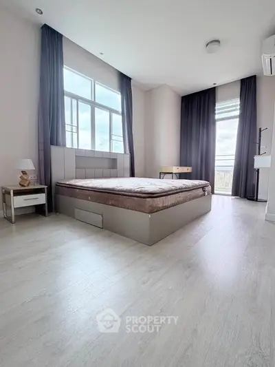Spacious bedroom with modern decor and large windows offering natural light.