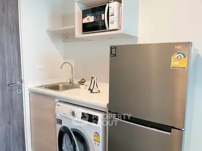 Modern compact kitchen with stainless steel fridge, washing machine, and microwave in a sleek design.